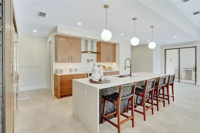 kitchen featuring a breakfast bar area, backsplash, a sink, modern cabinets, and wall chimney exhaust hood