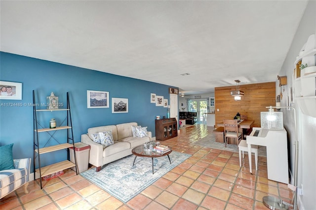 tiled living room with french doors, ceiling fan, and wooden walls