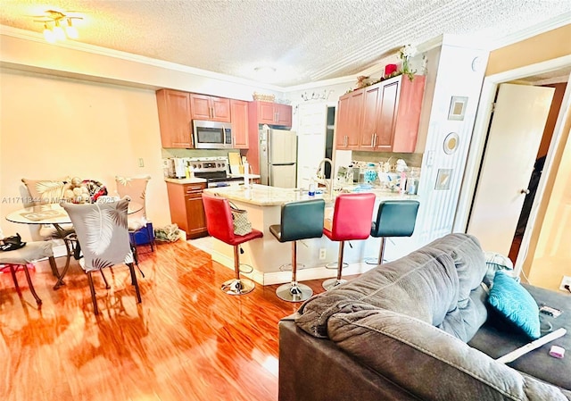 kitchen featuring crown molding, light wood-type flooring, a textured ceiling, appliances with stainless steel finishes, and a breakfast bar area