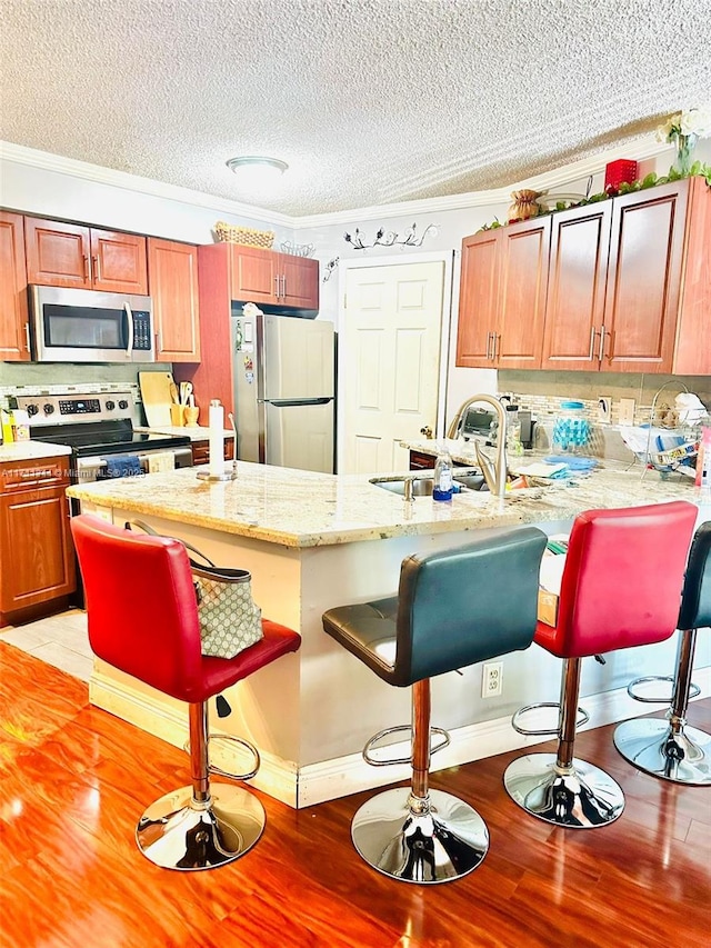 kitchen featuring a kitchen bar, ornamental molding, a textured ceiling, and appliances with stainless steel finishes