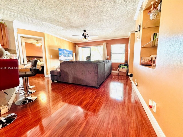 living room with crown molding, ceiling fan, wood-type flooring, and a textured ceiling