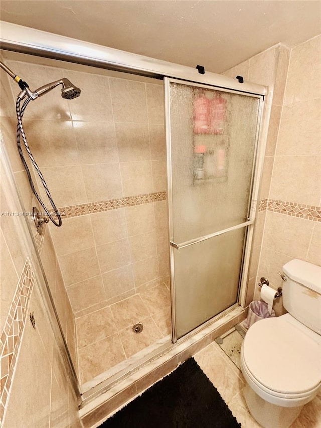 bathroom with tile patterned flooring, toilet, tile walls, and a shower with shower door