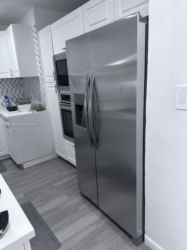 kitchen featuring backsplash, white cabinets, stainless steel appliances, and light hardwood / wood-style floors