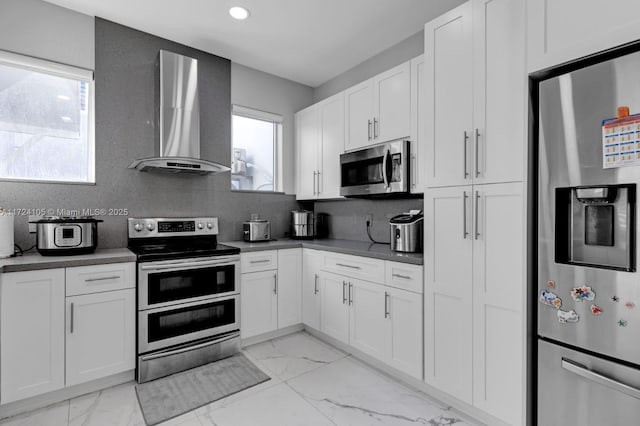 kitchen featuring white cabinets, stainless steel appliances, tasteful backsplash, and wall chimney exhaust hood