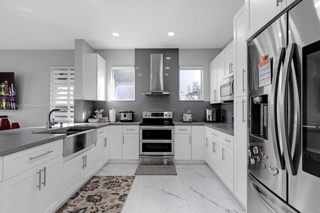 kitchen with white cabinets, appliances with stainless steel finishes, wall chimney range hood, and sink