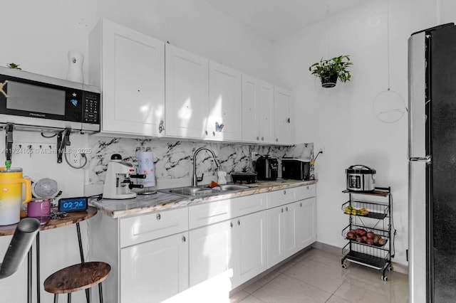 kitchen with light stone countertops, refrigerator, sink, white cabinetry, and backsplash