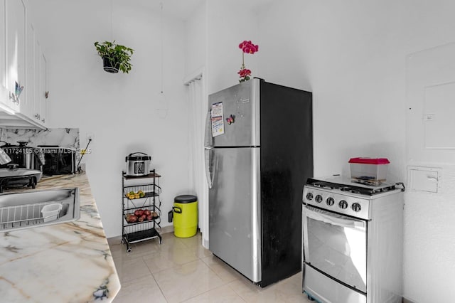 kitchen featuring stainless steel appliances, sink, white cabinets, light tile patterned floors, and decorative backsplash