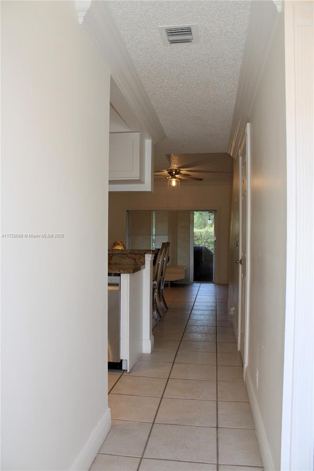 hall with light tile patterned floors, visible vents, a textured ceiling, and baseboards