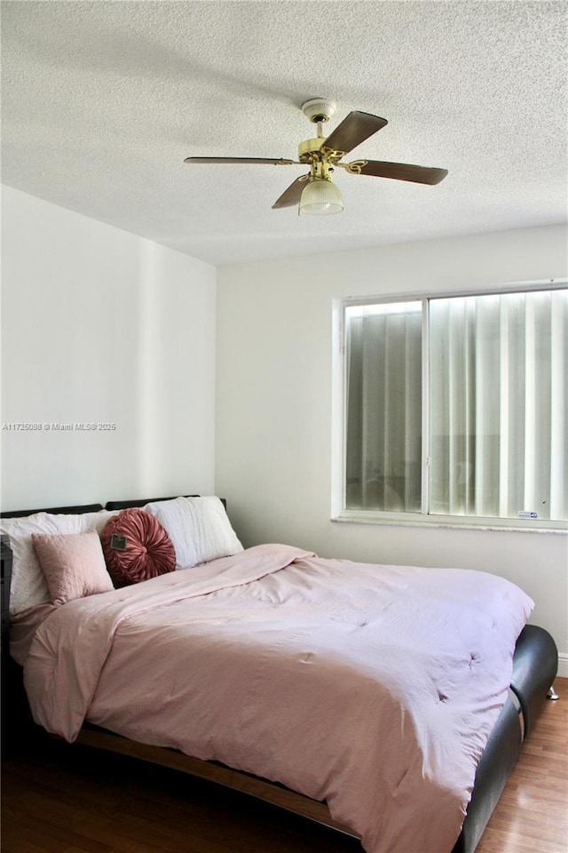 bedroom featuring a ceiling fan, wood finished floors, and a textured ceiling