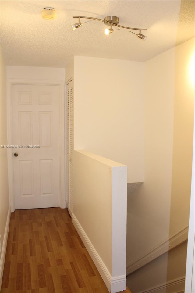 hallway featuring a textured ceiling, baseboards, and wood finished floors