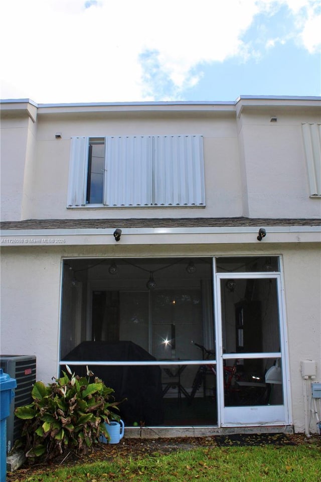 back of house with central air condition unit, a sunroom, and stucco siding