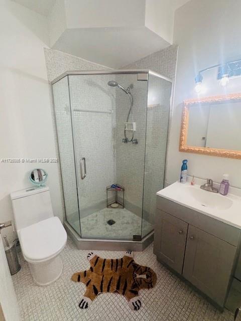 bathroom with tile patterned floors, vanity, toilet, and a shower with door