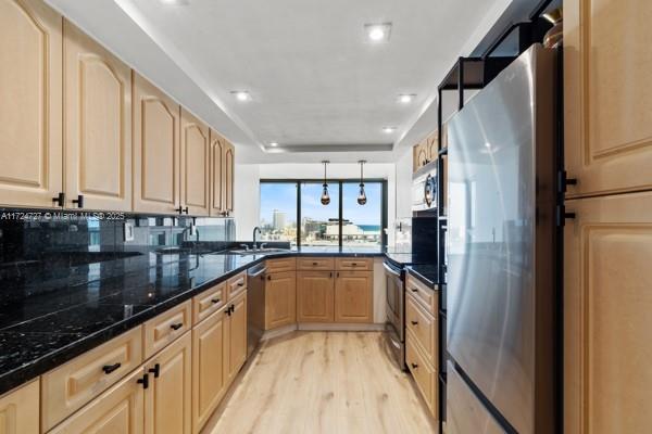 kitchen featuring stainless steel appliances, hanging light fixtures, light brown cabinets, and light hardwood / wood-style floors