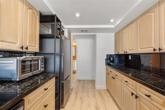 kitchen with dark stone counters, light hardwood / wood-style flooring, decorative backsplash, and light brown cabinets