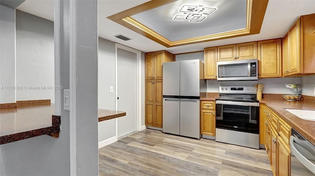 kitchen with appliances with stainless steel finishes, light hardwood / wood-style floors, crown molding, and a tray ceiling