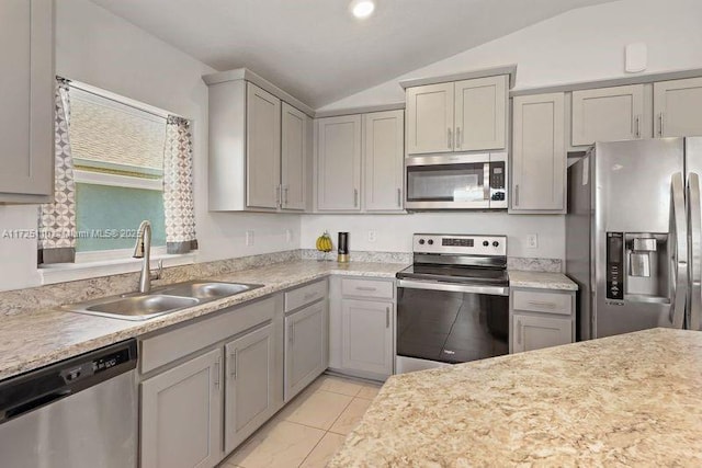 kitchen with appliances with stainless steel finishes, light tile patterned floors, vaulted ceiling, and sink