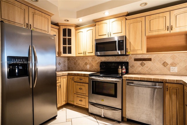 kitchen featuring stainless steel appliances, tile counters, light brown cabinetry, and backsplash