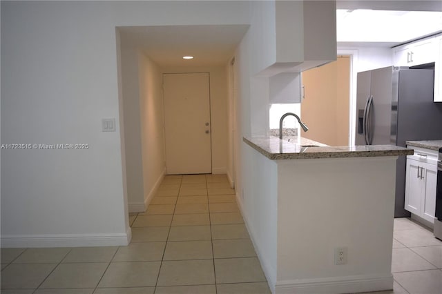 kitchen featuring sink, light stone countertops, light tile patterned floors, white cabinetry, and stainless steel fridge with ice dispenser