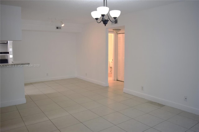 tiled spare room featuring a chandelier