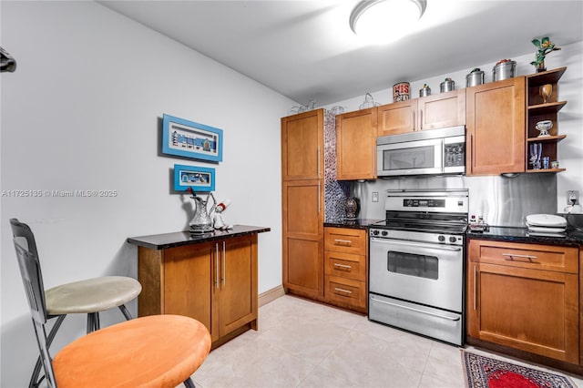 kitchen with backsplash, light tile patterned floors, dark stone counters, and appliances with stainless steel finishes