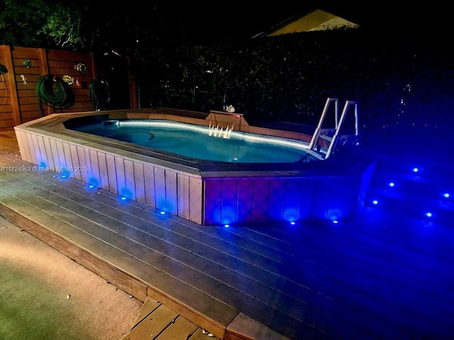 pool at twilight with a wooden deck, fence, and a hot tub