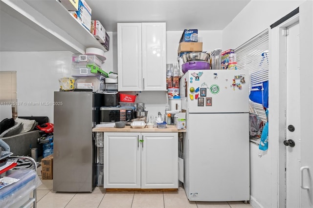 kitchen featuring stainless steel refrigerator, white refrigerator, light tile patterned floors, and white cabinetry