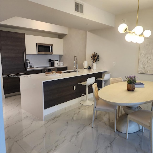 kitchen featuring sink, white cabinetry, kitchen peninsula, hanging light fixtures, and dark brown cabinetry