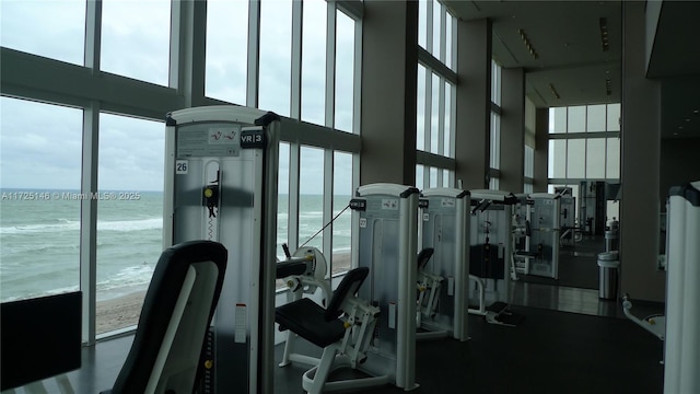 workout area featuring a towering ceiling, a view of the beach, and a water view