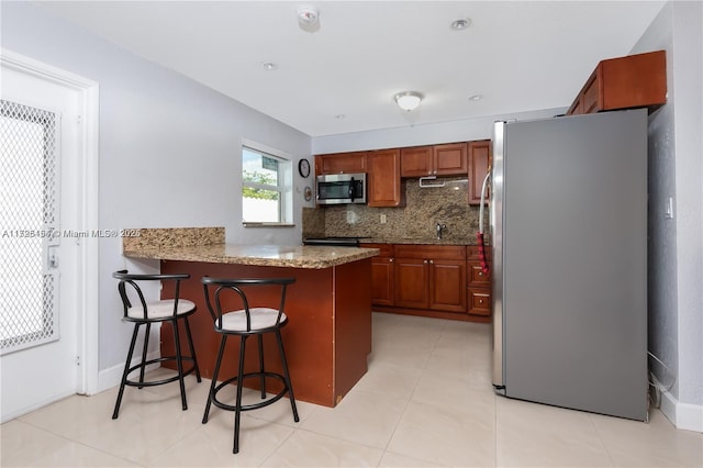 kitchen featuring light stone counters, kitchen peninsula, backsplash, a breakfast bar, and appliances with stainless steel finishes