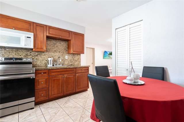 kitchen with dark stone countertops, sink, stainless steel range with electric cooktop, light tile patterned flooring, and tasteful backsplash