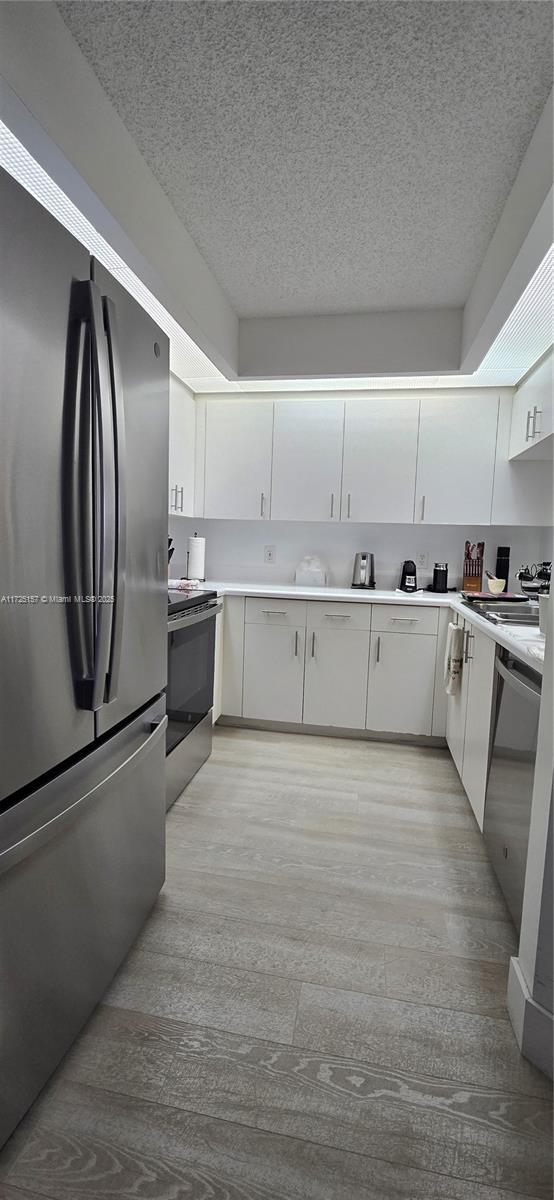 kitchen with stainless steel appliances, white cabinets, and light hardwood / wood-style flooring