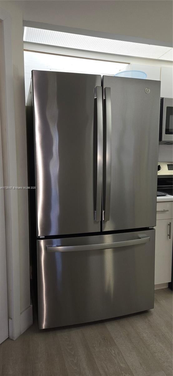 interior details with appliances with stainless steel finishes, white cabinets, and hardwood / wood-style floors