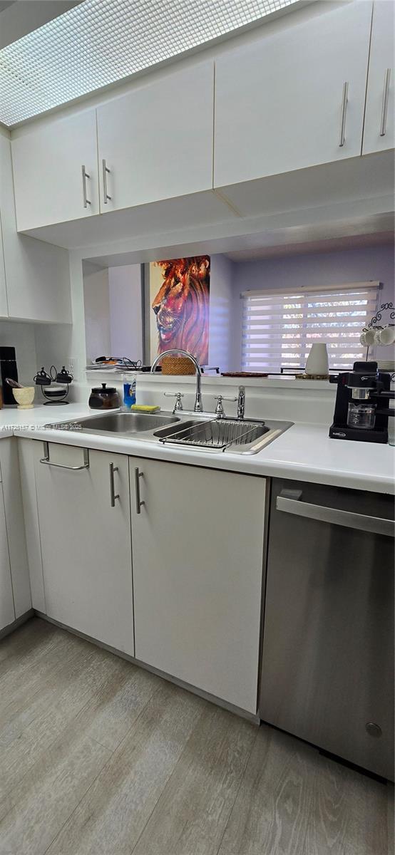 kitchen featuring white cabinets, light hardwood / wood-style floors, stainless steel dishwasher, and sink