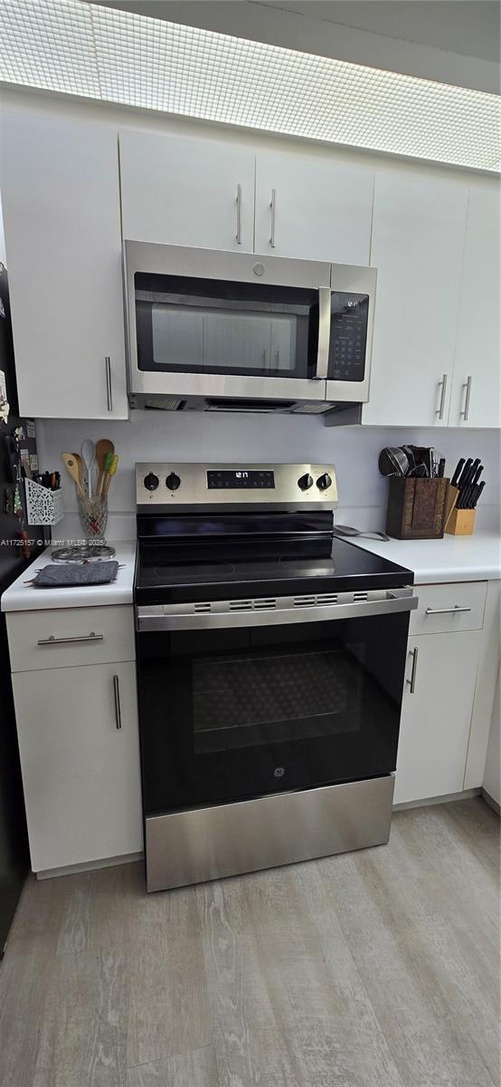 kitchen with stainless steel appliances, white cabinetry, and light wood-type flooring