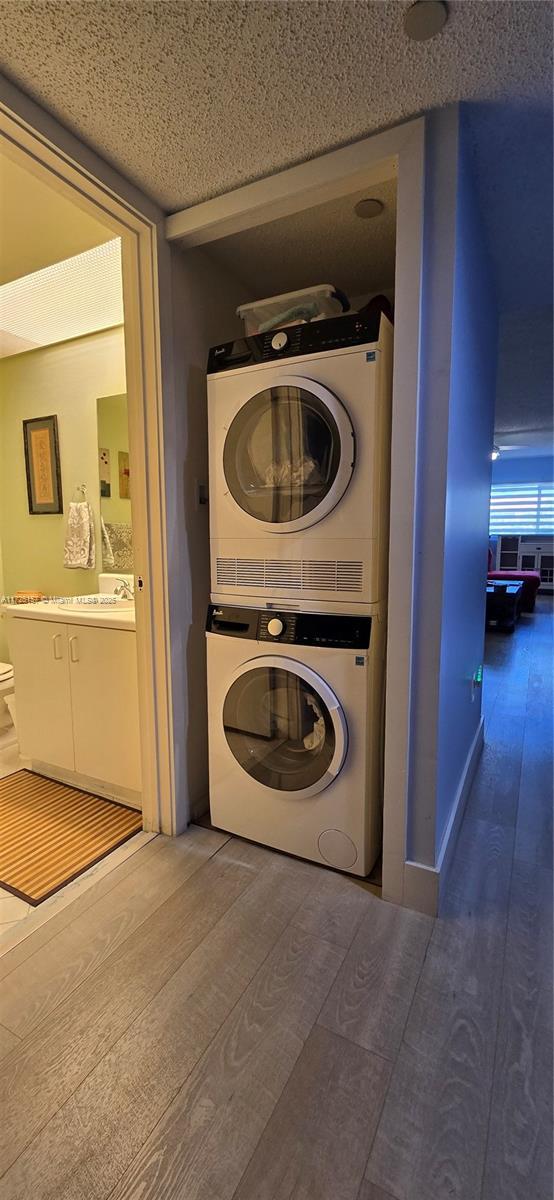 clothes washing area featuring dark wood-type flooring, a textured ceiling, and stacked washer and clothes dryer