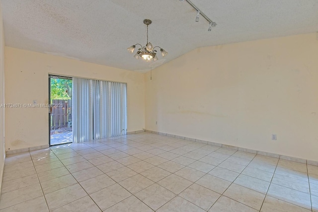 unfurnished room with rail lighting, light tile patterned floors, a textured ceiling, an inviting chandelier, and lofted ceiling