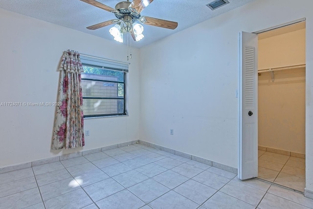 unfurnished bedroom featuring a textured ceiling, a closet, ceiling fan, a walk in closet, and light tile patterned flooring