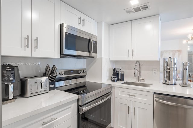 kitchen featuring sink, appliances with stainless steel finishes, light stone counters, and white cabinetry