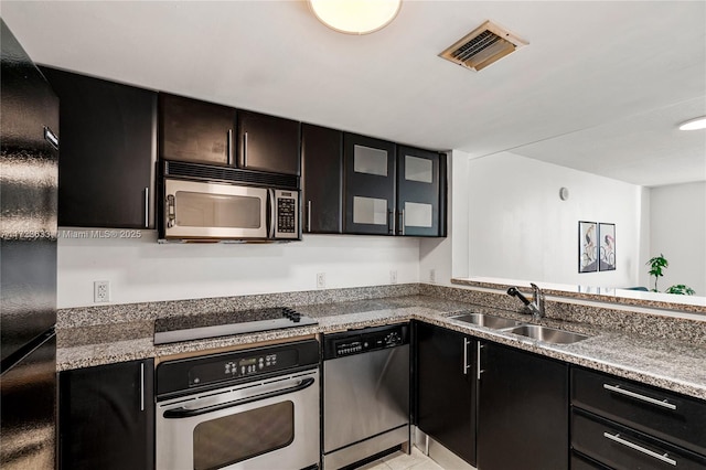 kitchen with sink, stainless steel appliances, dark stone countertops, and light tile patterned flooring