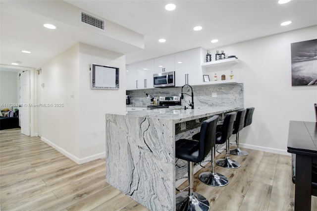 kitchen featuring stainless steel appliances, white cabinets, light wood-type flooring, kitchen peninsula, and a breakfast bar area