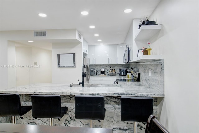 bar with white cabinetry, backsplash, light stone counters, and appliances with stainless steel finishes