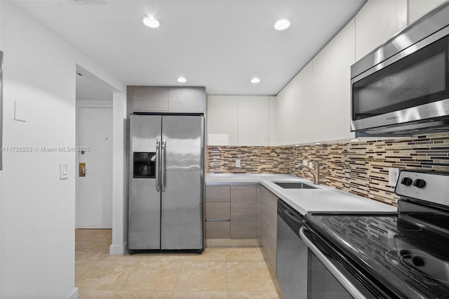 kitchen with stainless steel appliances, sink, white cabinetry, light tile patterned flooring, and tasteful backsplash