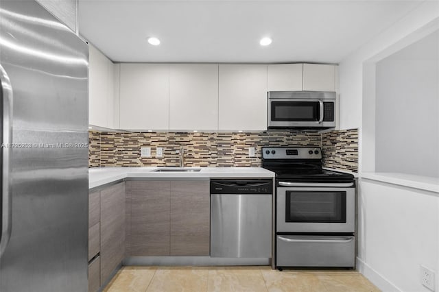 kitchen featuring stainless steel appliances, sink, white cabinetry, light tile patterned floors, and tasteful backsplash