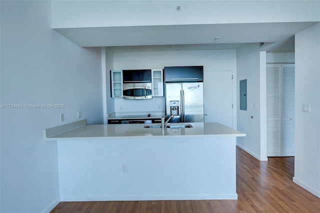 kitchen with kitchen peninsula, electric panel, appliances with stainless steel finishes, wood-type flooring, and sink