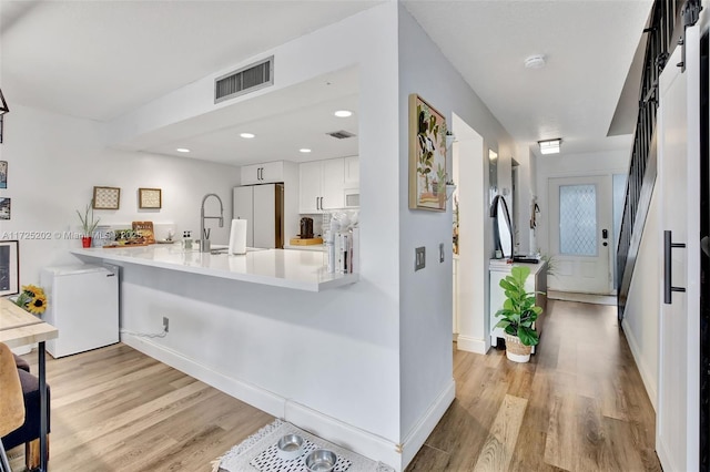 kitchen featuring white cabinets, light wood-type flooring, white appliances, and kitchen peninsula