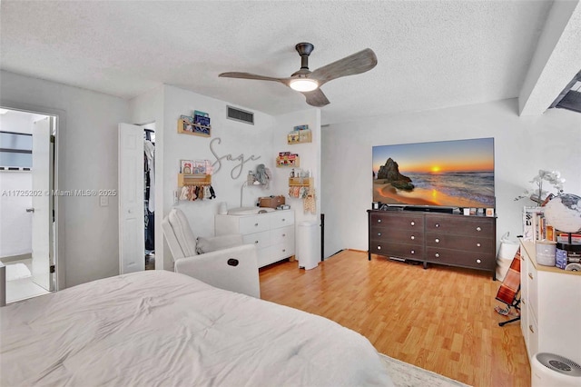 bedroom featuring a textured ceiling, ceiling fan, light hardwood / wood-style floors, and connected bathroom