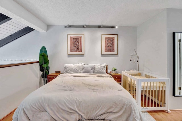 bedroom with a textured ceiling, wood-type flooring, and vaulted ceiling with beams