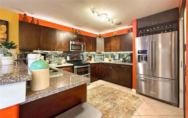 kitchen with a textured ceiling, tasteful backsplash, light tile patterned floors, dark brown cabinets, and appliances with stainless steel finishes