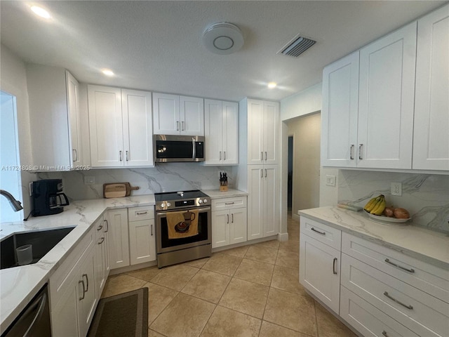 kitchen featuring backsplash, white cabinetry, appliances with stainless steel finishes, light tile patterned flooring, and sink