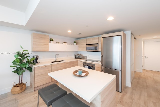 kitchen with sink, light brown cabinets, black appliances, a kitchen island, and a breakfast bar